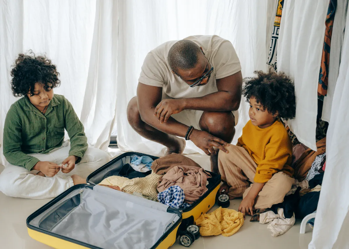 A parent and two children packing a suitcase together on the floor
